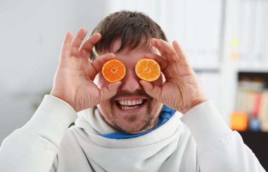 Male hands hold a cut fruit at eye level instead of glasses. The theme of a healthy diet for withdrawal activities and belief in diet achievements in business and education.