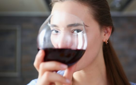 Beautiful smiling brunette woman hold in arms glass of red wine at kitchen table portrait. Vine cabernet merlot sauvignon lips beauty concept