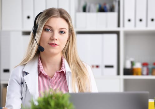 A beautiful feminine blonde doctor talking to patient over wireless headset advises a medical problem the formation of remote education internship callcenter specialist