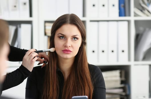 Beautiful brunette businesswoman hold in arm phone at workplace portrait wile getting makeup preparing for tv air. Negotiate meeting job busy life style device store concept