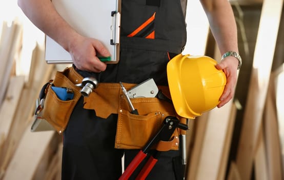 Handyman with hands on waist and tool belt with construction tools against wood background. DIY tools and manual work concept