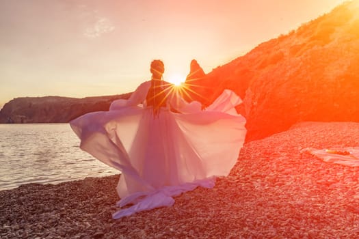 Mysterious woman silhouette long hair walks on the beach ocean water, sea nymph wind listens to the wave. Throws up a long white dress, a divine sunset. Artistic photo from the back without a face.