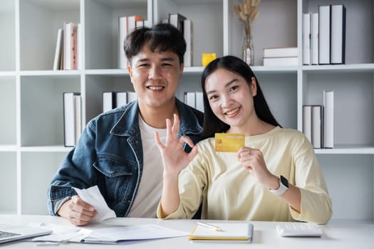 Smiling couple sitting and managing bills at home, paying by credit card. Happy man and woman pay bills and manage budget. couple checking accounts and bills while looking at receipt.