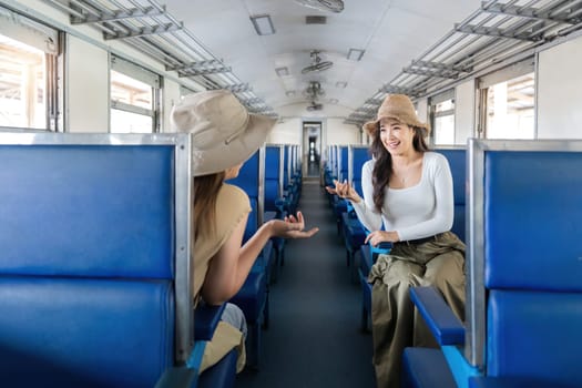 Two women friend talk and laugh while travel by train, railroad trip concept.