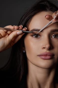 beauty professional woman holding eyelash tweezers while posing on black background. close-up