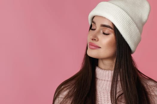 portrait of young woman in white hat, pink sweater losing eyes in pleasure on pastel pink background. copy space