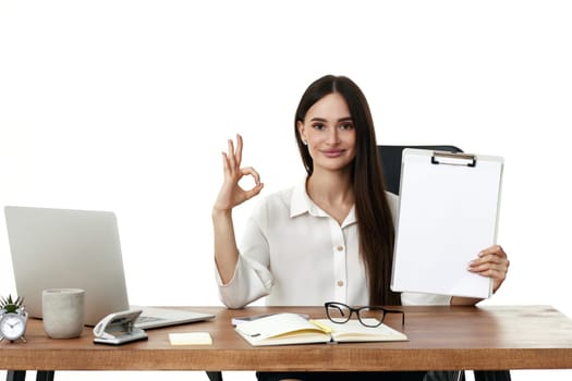 positive businesswoman showing empty clipboard and Ok gesture in the office