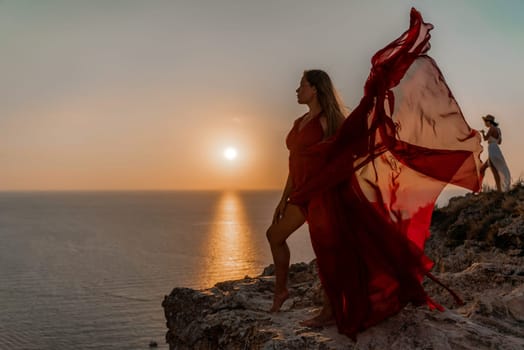 Woman sunset sea red dress, side view a happy beautiful sensual woman in a red long dress posing on a rock high above the sea on sunset