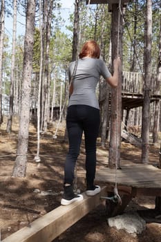 teenage girl walks along wooden structures in a rope training camp in the forest.