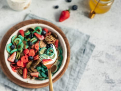 Trendy food - pancake cereal. Bowl of colorful mini cereal pancakes in spoon with milk. Tiny pancakes with natural color - green matcha, turquose spirulina, blue pea, red fragon fruit. Copy space