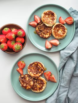 Sweet cheese pancakes on plate served strawberries. Cottage cheese pancakes, syrniki, ricotta fritters, curd fritters. Top view or flat lay. Vertical.