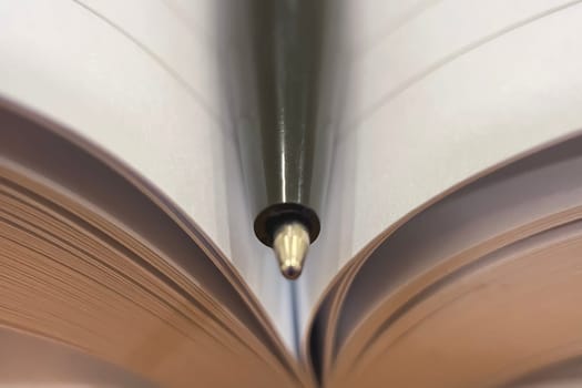Knowledge at Your Fingertips.Captured by a sleek pen resting in an open book. The symmetrical layout of the pages directs attention to the writing instrument, evoking a journey filled with education, wisdom, and stories.