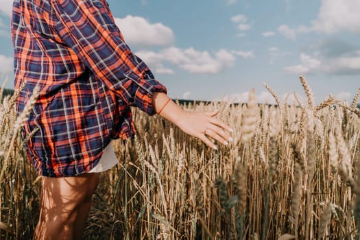 A woman's hand reaches out towards the golden wheat stalks in a field under a blue sky.