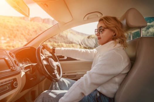 A woman in sunglasses drives a car, her hand on the steering wheel. Sunlight shines through the windshield.