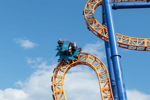 Helsinki, Finland - 19 AUGUST 2024: Linnanmaki amusement park with Ride roller coaster Kirnu in motion, blue sky on a background, happy people