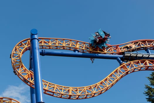 Helsinki, Finland - 19 AUGUST 2024: Linnanmaki amusement park with Ride roller coaster Kirnu in motion, blue sky on a background, happy people
