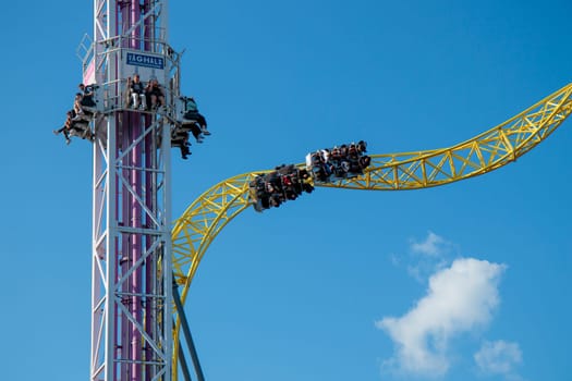 Helsinki, Finland - 19 AUGUST 2024: Linnanmaki amusement park with roller coaster Ukko and rides tower Raketti in motion, blue sky on a background, happy people