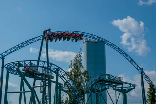 Helsinki, Finland - 19 AUGUST 2024: Linnanmaki amusement park with roller coaster Taiga in motion, blue sky on a background, happy people