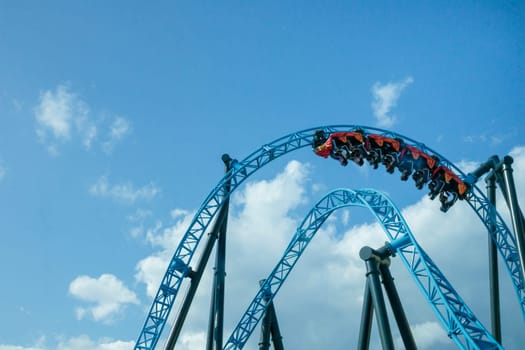 Helsinki, Finland - 19 AUGUST 2024: Linnanmaki amusement park with roller coaster Taiga in motion, blue sky on a background, happy people