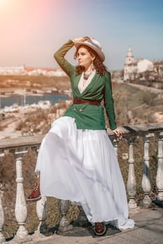 Woman walks around the city, lifestyle. A young beautiful woman in a green jacket, white skirt and hat is sitting on a white fence with balusters overlooking the sea bay and the city