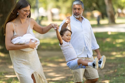 Happy family is enjoying a sunny day at the park, swinging their son between them as they walk