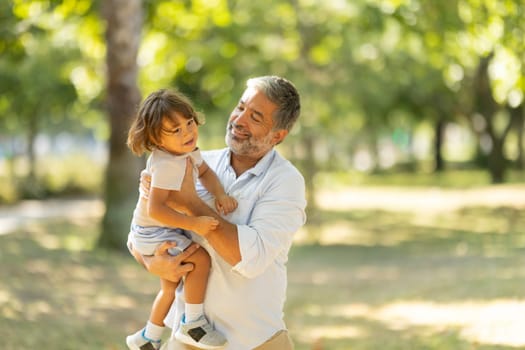 Father is lifting his young son into the air while enjoying a sunny day outdoors at the park