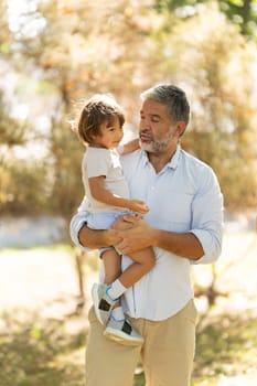 Grandfather is holding his grandson in his arms, enjoying a beautiful sunny day at the park