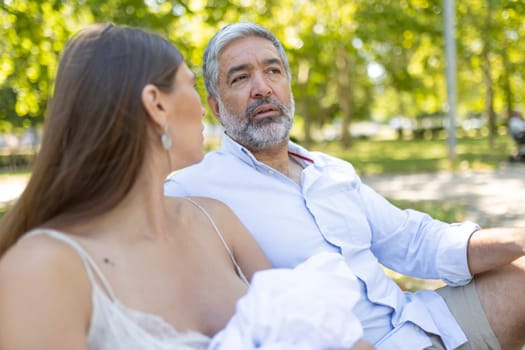 Young mother and grandfather are sitting on a park bench, enjoying the summer day with their baby