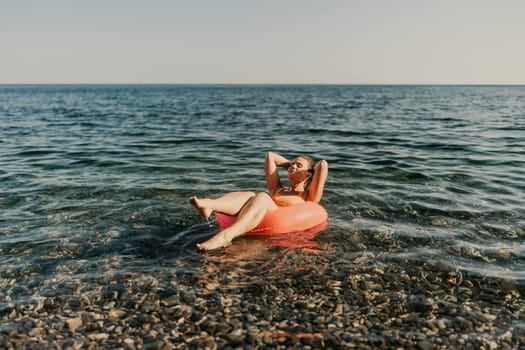 A woman is floating on a red inflatable tube in the ocean. The water is calm and the sky is clear. The woman is enjoying her time in the water