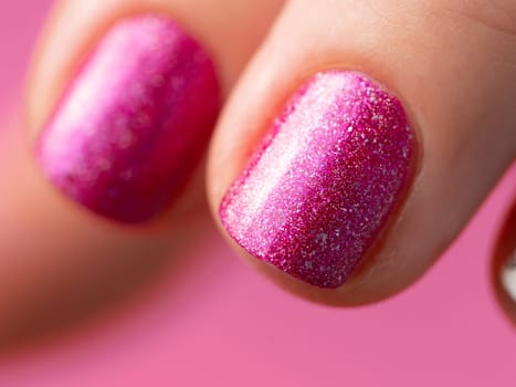 Female hand with pink manicure. Close up of short fingernail with pink holographic nail polish gel lacquer. Aesthetic visual of red violet holo manicure