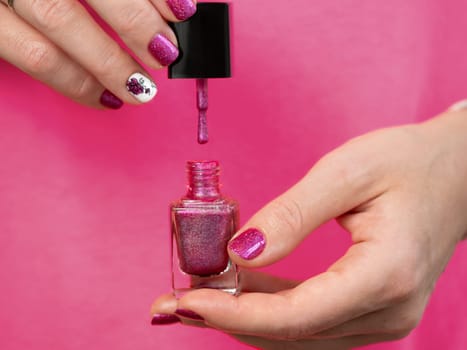 Female hands with pink manicure has pink purple nail polish bottle. Woman holding pink holographic nail polish lacquer brush. Aesthetic visual of red violet manicure with lady silhouette stamping