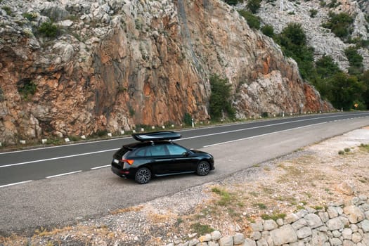 A black car parked near a rocky landscape along a winding mountain road.