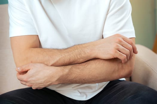 The man is sitting on a gray couch and holding his belly. Medicine and health concept, stomach problems. The man suffers from stomach ache, gastric problems. Abdominal pain, suffering and pain.