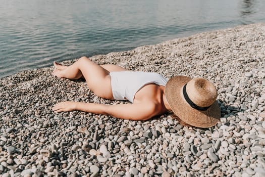 A woman is laying on the beach wearing a straw hat. She is wearing a white bikini top and white bikini bottoms