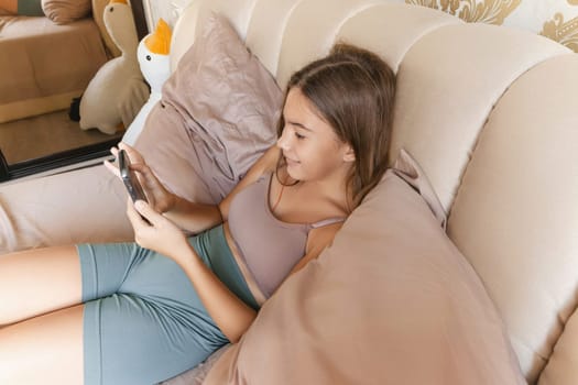 A girl is laying on a bed with a cell phone in her hand. She is smiling and she is enjoying herself