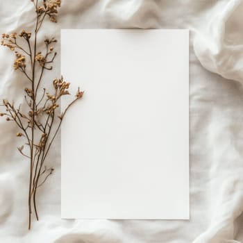 A piece of blank paper lies on a textured fabric backdrop surrounded by delicate dried flowers, creating an inviting space for writing or artistic projects.