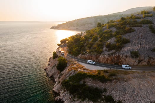Scenic coastal road travels along the waterfront at sunset in a beautiful mountainous region.
