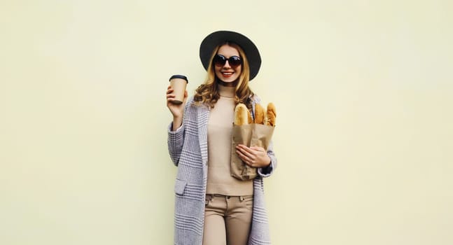 Portrait of beautiful happy young woman holding grocery shopping paper bag with white bread baguette drinking coffee after bakery on white background