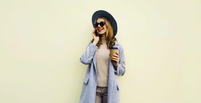 Fashionable happy smiling young woman calling on phone, stylish girl talking on the smartphone with cup of coffee in round hat standing on white background