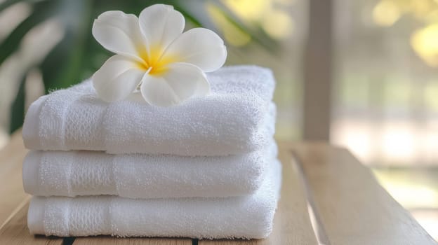 Stack of white towels with plumeria flower on wooden table, spa and relaxation concept.