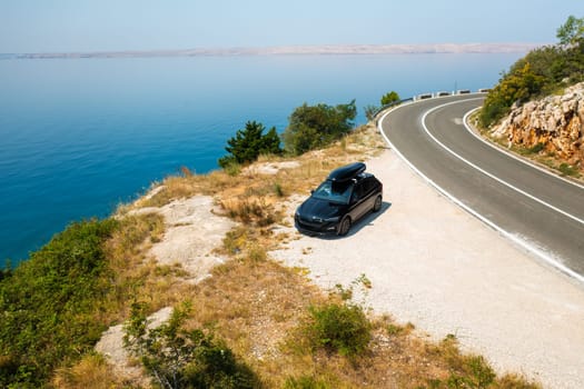 Car with a roof box stands on the side of a cliff and beautiful rocks in the background.
