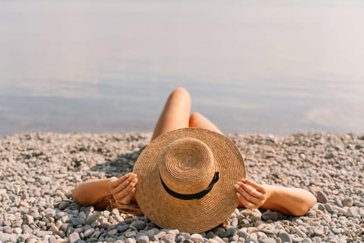 A woman is laying on the beach wearing a straw hat. She is relaxed and enjoying the sun