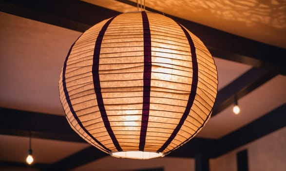 A close-up of a paper lantern hanging from the ceiling. The lantern is round and has a light brown color. The lantern is made of paper and has a pattern of vertical lines