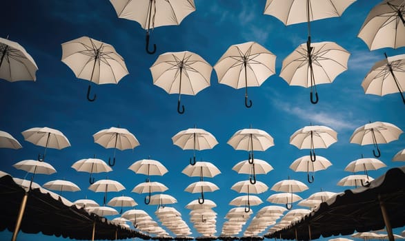 Many white umbrellas hang upside down in rows against a bright blue sky. The umbrellas are suspended by their handles, creating a pattern of overlapping circles.