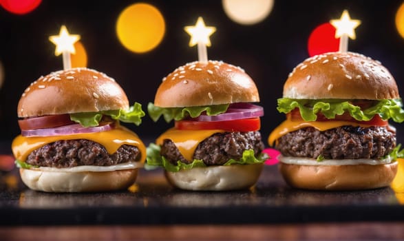 Three mini cheeseburgers are arranged in a row on a dark surface. Each burger is topped with lettuce, tomato, onion, and melted cheese. The burgers are lit by warm, blurry lights behind them.