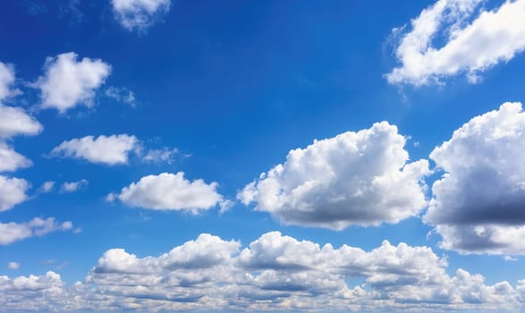A wide shot of a blue sky with scattered white clouds. The clouds are of various sizes, with some large and fluffy, and others smaller and more wispy
