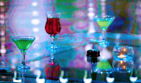 A close-up shot of three cocktails on a table, illuminated by vibrant neon lights in a dimly lit setting.