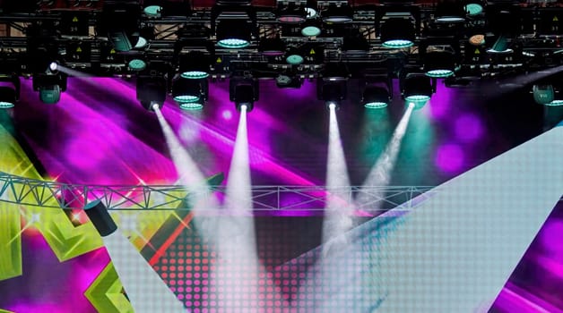 Vibrant purple stage lights and bright rays create an energetic atmosphere, perfect for concerts. The colorful lights draw audience attention to the stage, enhancing excitement and anticipation.