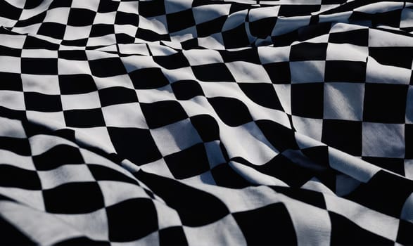 A close-up view of a black and white checkered flag lying flat in a bright, sunny area.