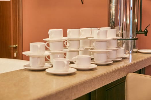 There is a neat stack of several coffee cups along with matching saucers beautifully arranged on a counter top